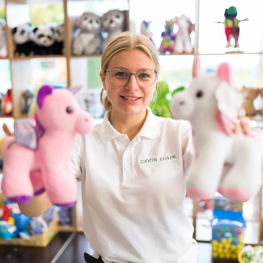 Ausbildung bei potts park: Junge Frau steht im Souvenirshop und hält zwei Kuscheltiere in die Kamera
