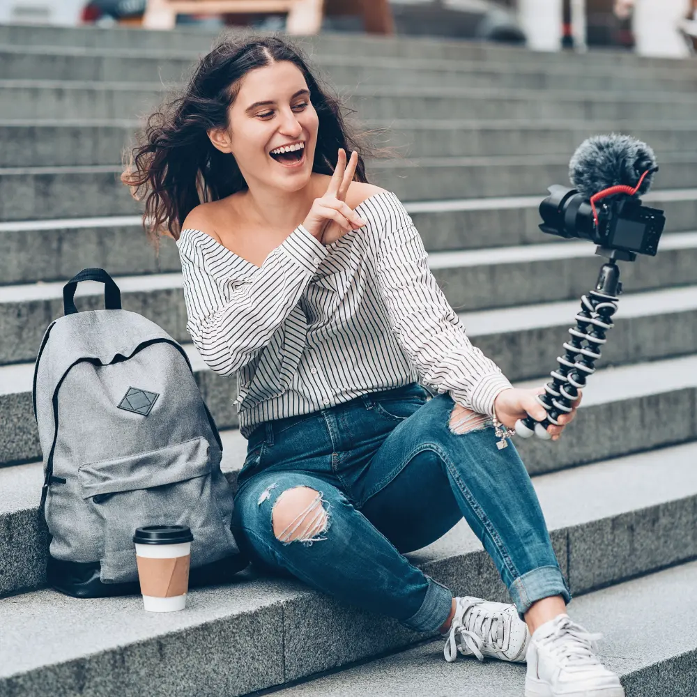 deine-mission Creator mit Selfie-Stick sitzt auf einer Steintreppe